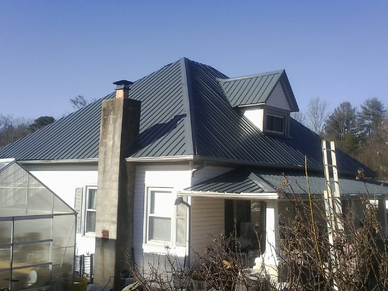 Dark blue standing seam metal roof on a white farmhouse with dormer — Slate & Tile Roof Repair by Roofing Brothers in Berryton