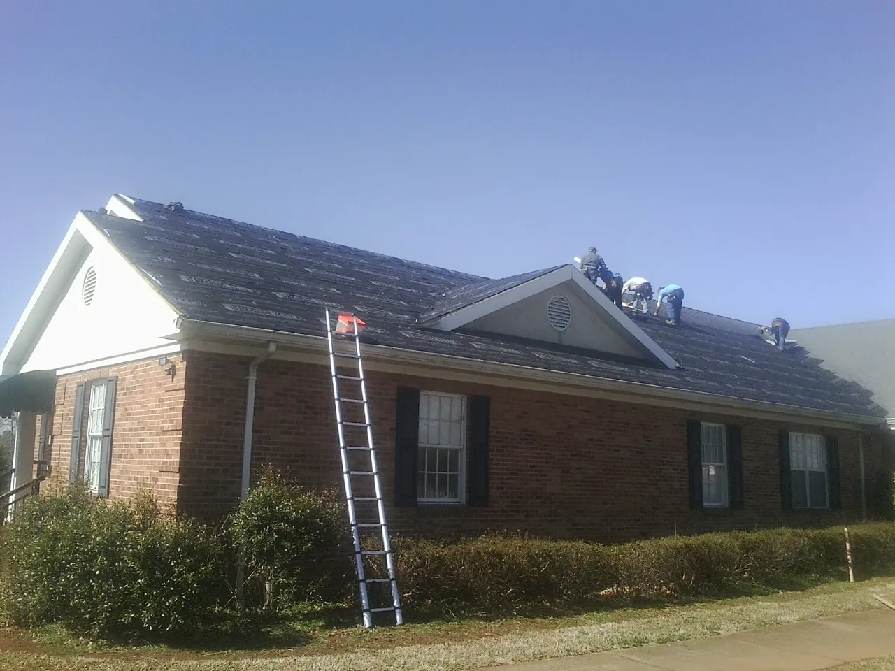 Crew tearing shingles off a brick ranch roof with a ladder set — Metal Roof Repair work by our crew in Berryton
