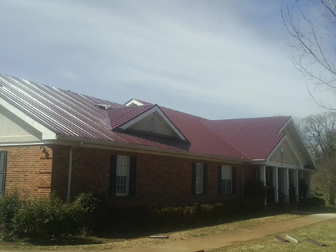 Red metal roof with gabled entries on a long brick building, from a Hail Damage Roof Repair job in Berryton