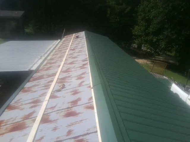 Old rusted panels beside newly installed green metal roofing — Wind Damage Roof Repair by Roofing Brothers in Berryton