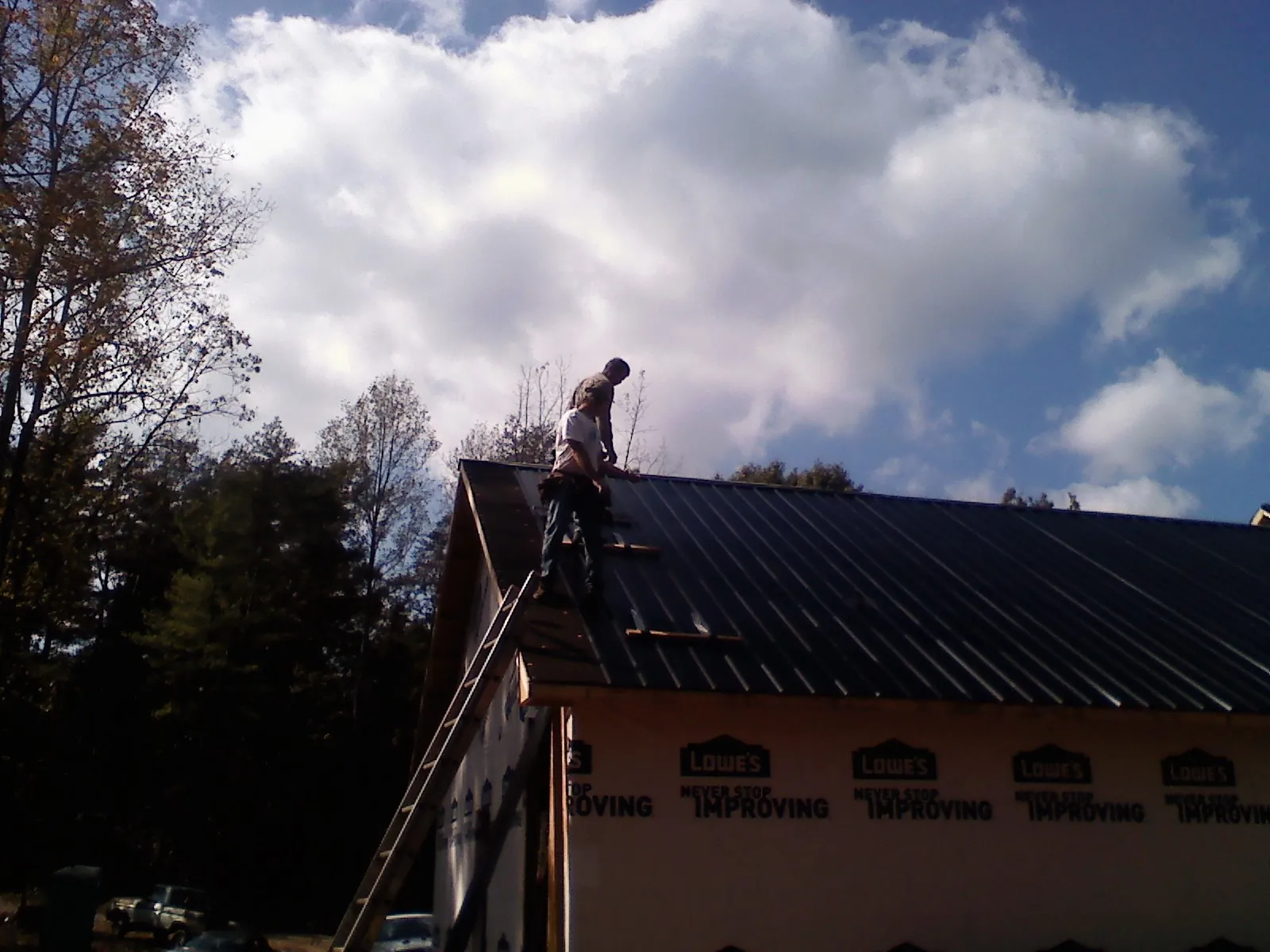 Roofer fastening dark metal panels high against a cloudy sky, from a Roof Inspection job in Berryton