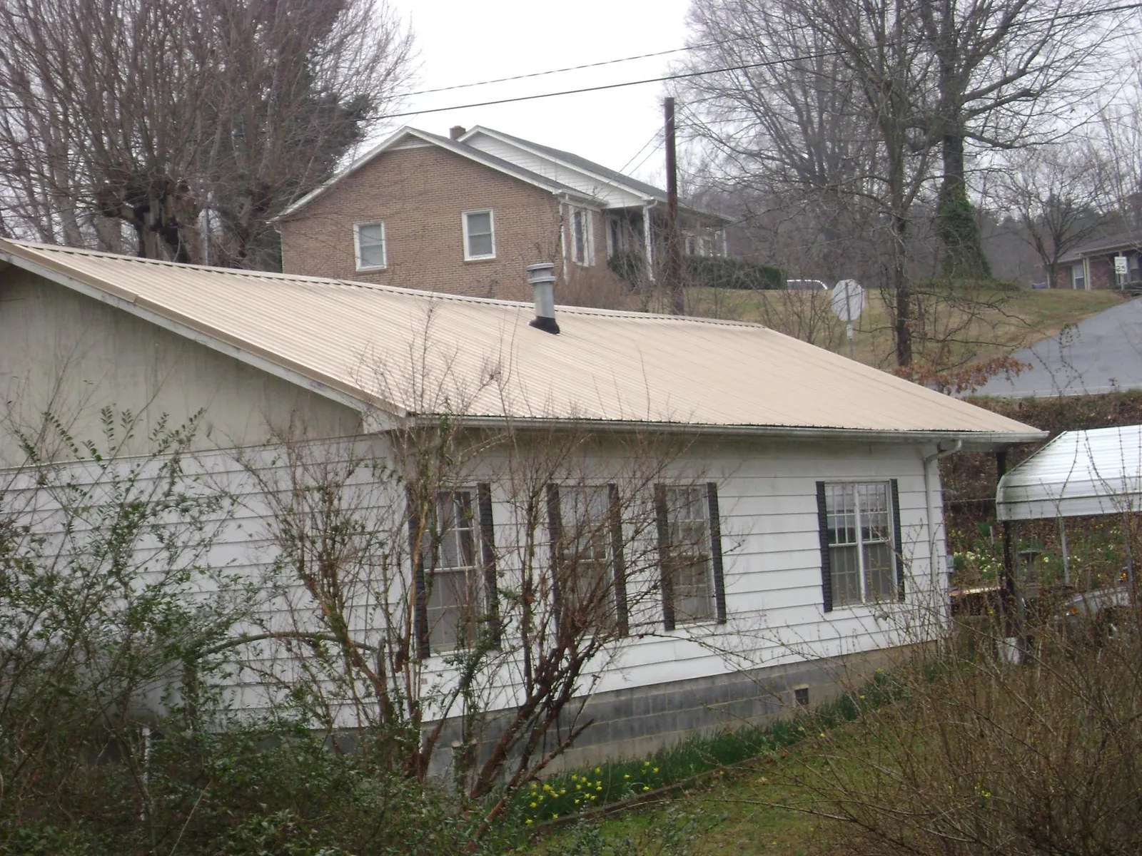 Tan metal roof on a white sided house set into a hillside — Commercial Roofing by Roofing Brothers in Berryton