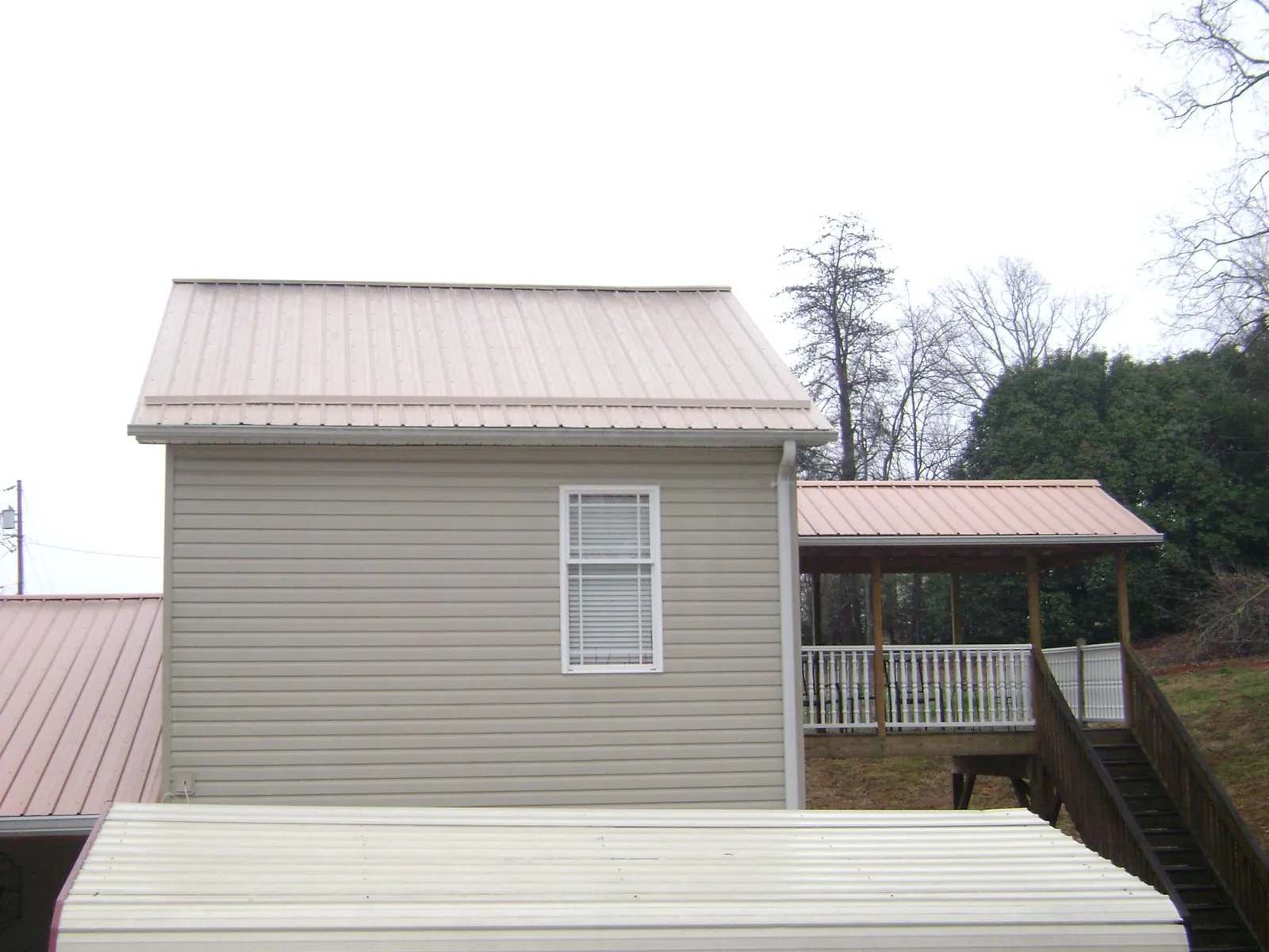 Tan metal roofs on a two story addition and attached porch, from a Roof Replacement job in Berryton